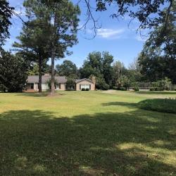 Wide green lawn with tall trees leading to house and detached garage under blue sky.