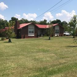 Brick house with red roof and neatly mowed front lawn on sunny day with scattered clouds.